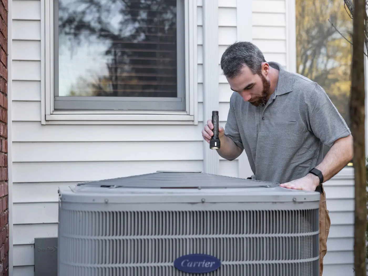 Technician inspecting an outdoor air conditioning unit beside a house
